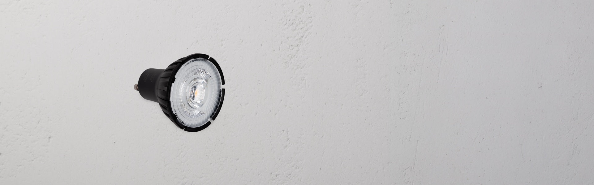 Close-up of a round LED bulb with a black base, mounted on a textured white wall.