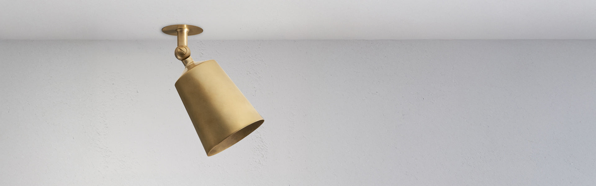 A sleek, modern brass pendant light hangs from a ceiling, casting a warm glow against a plain white wall.