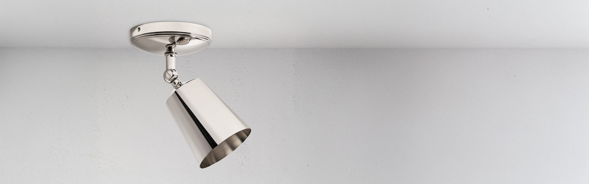 A minimalist polished nickel ceiling light fixture hangs from a smooth white ceiling, casting soft illumination.