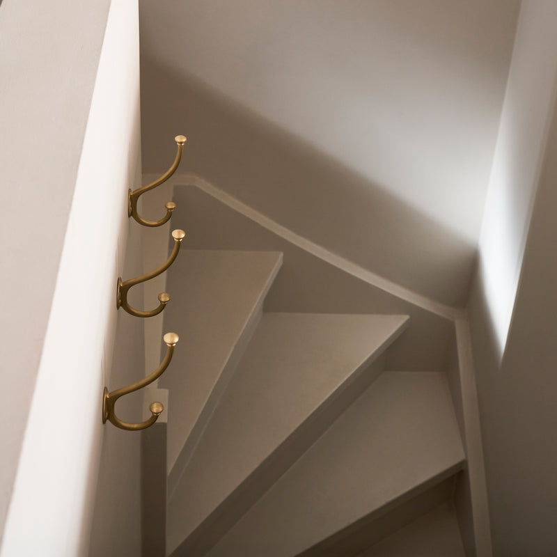 A minimalist staircase with curved steps, featuring three elegant gold hooks mounted on a white wall. Soft light casts gentle shadows.