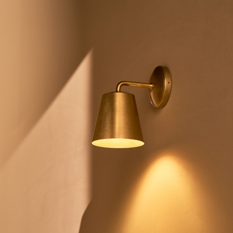 A sleek, brass wall sconce casts a warm glow onto a softly lit wall, highlighting its modern design and elegant curves.