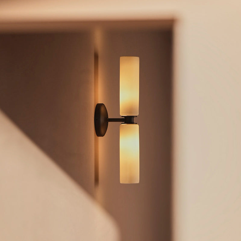 Sleek wall sconce featuring two vertical, frosted glass light shades mounted on a black base, casting warm ambient light.