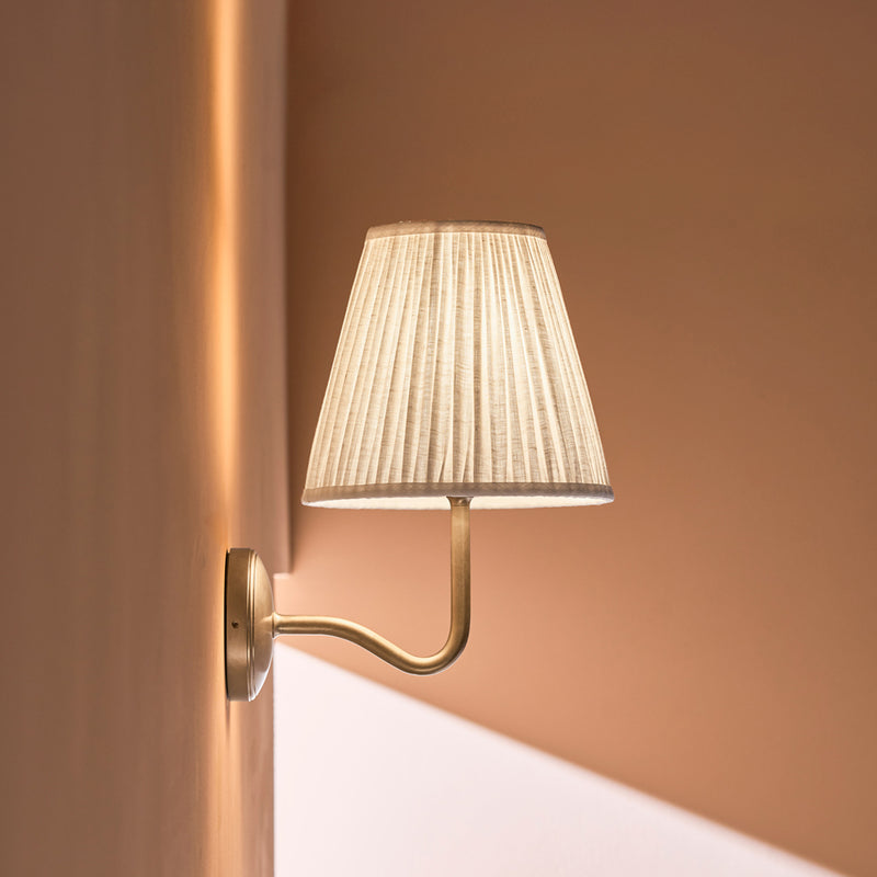 A modern wall-mounted lamp with a textured fabric shade, casting soft light against a warm-toned wall.