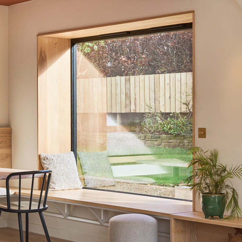 Cozy interior scene featuring a large window with garden view, wooden bench, potted plants, and modern furniture elements.