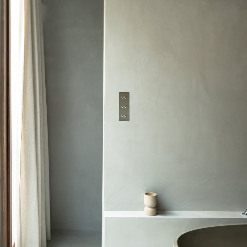 A modern bathroom with gray plaster walls, a minimalist tub, and soft curtains allowing natural light to enter.