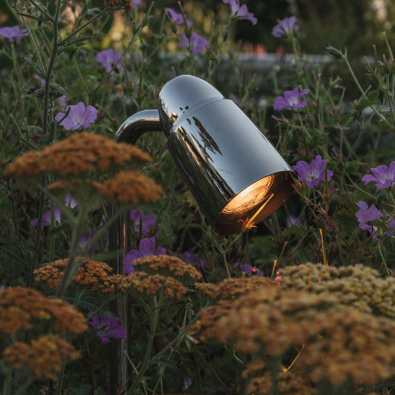 A sleek garden lamp emits warm light amidst vibrant flowers, enhancing the serene outdoor atmosphere.