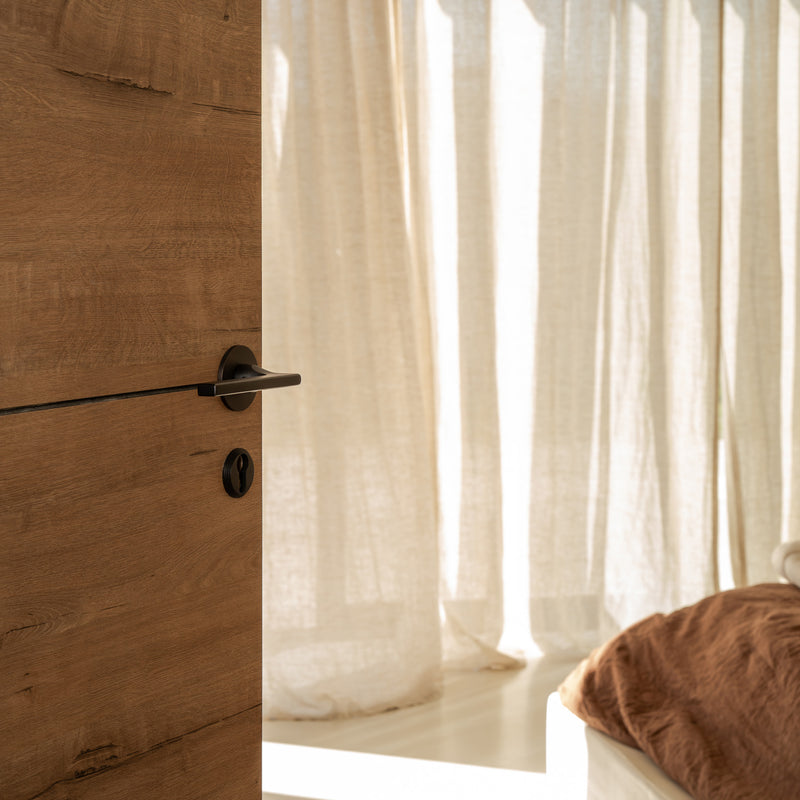 A partially open wooden door reveals soft, flowing curtains and a cozy bed, illuminated by warm sunlight streaming in.