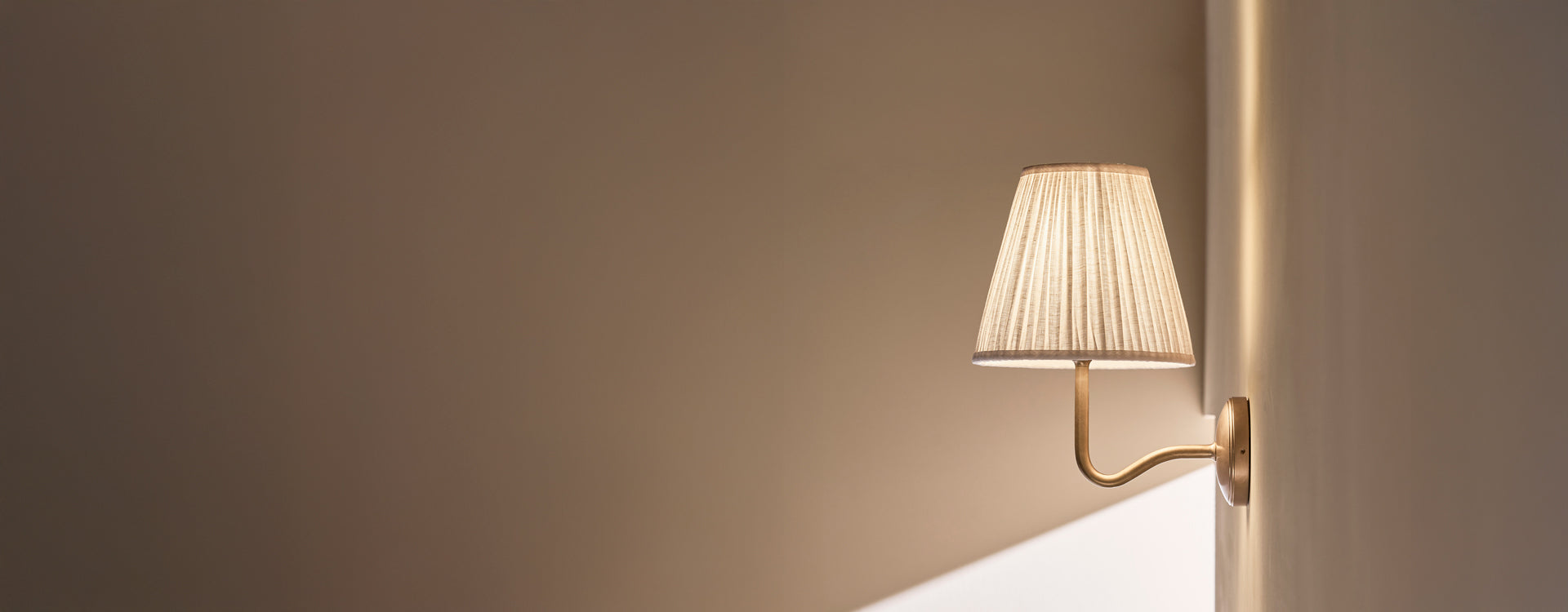 A stylish wall sconce with a pleated lampshade casts soft light against a minimalist beige wall, enhancing the room's elegance.

