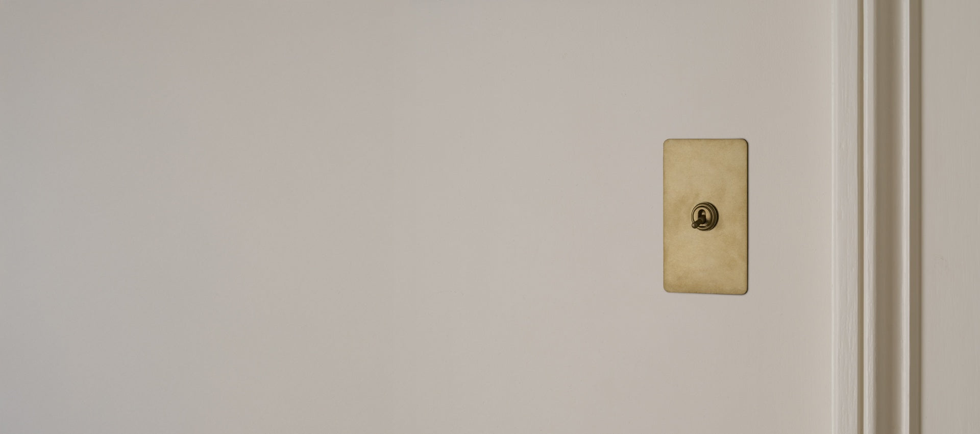 A vintage brass lightswitch set against a pale wall, featuring a rectangular plate and a circular key opening.
