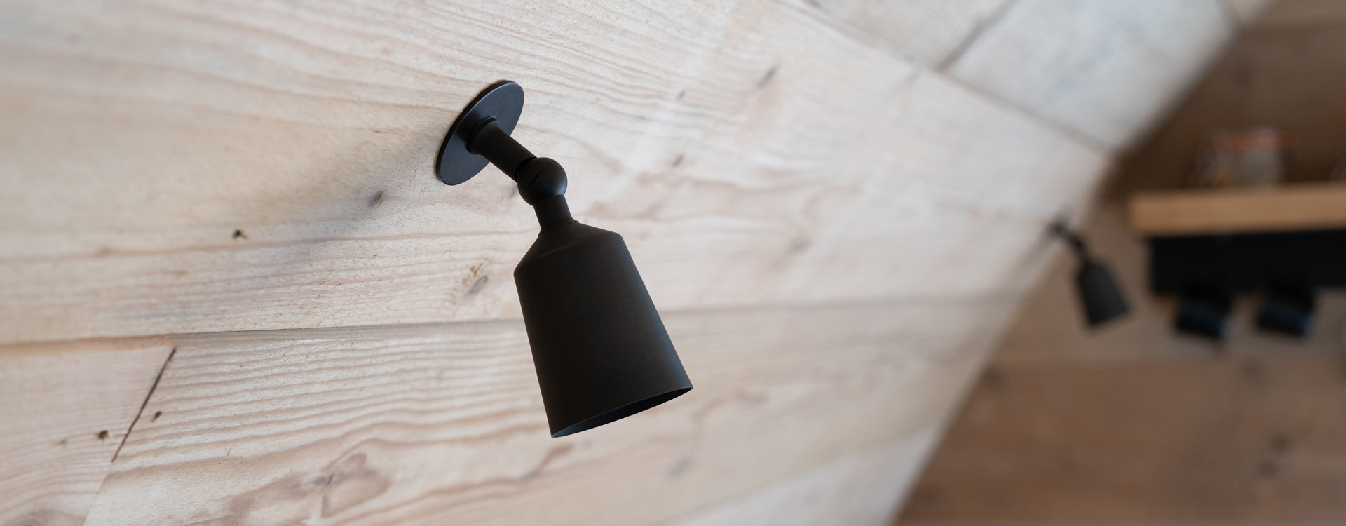 Black wall-mounted light fixture installed on a rustic wooden wall, featuring a sleek and modern design.
