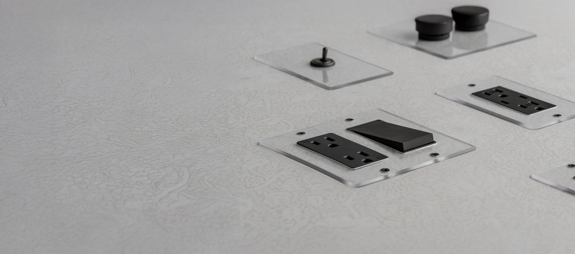 Close-up of multiple black electrical outlets and a switch mounted on a white textured surface, featuring clear protective covers.
