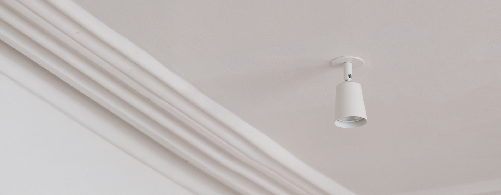 A minimalist white ceiling light fixture hangs from a smooth white ceiling, casting soft illumination.
