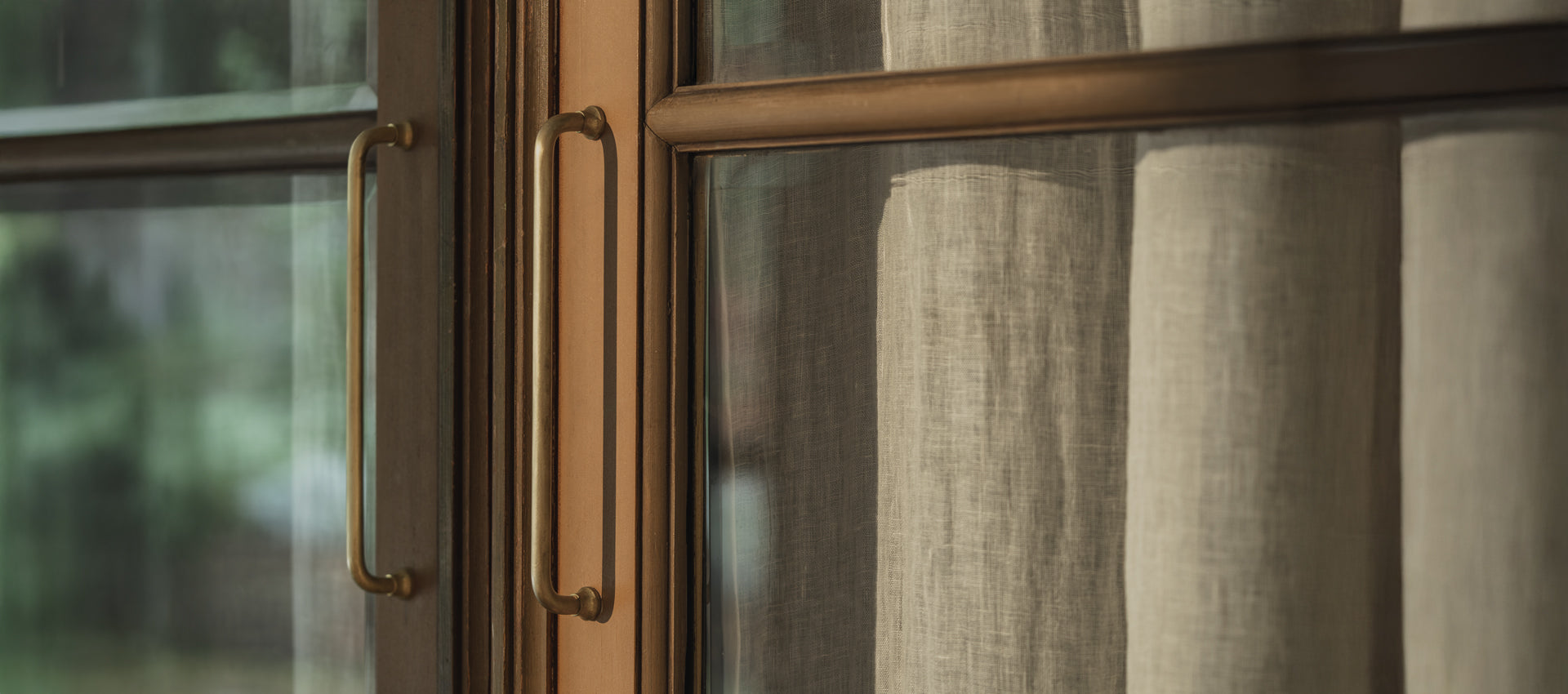 Close-up of elegant brass handles on a glass door, showcasing modern design against a blurred outdoor background.
