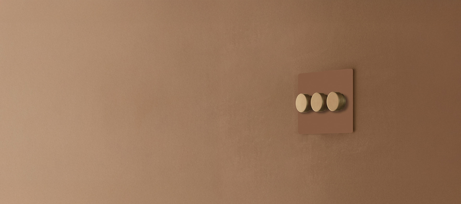 A modern light switch with three round gold buttons on a matte brown wall, showcasing sleek minimalist design.
