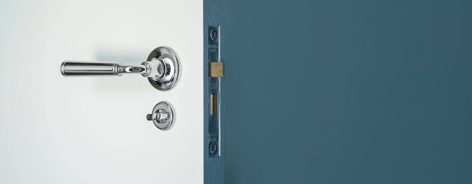 Close-up of a polished chrome door handle and lock mechanism on a sleek, modern door with a simple white background.
