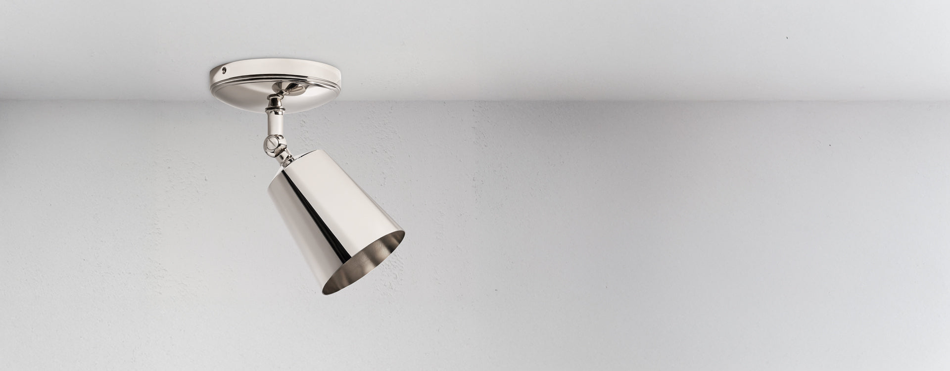 Modern chrome ceiling light with a angled shade, mounted on a round base against a textured white wall.
