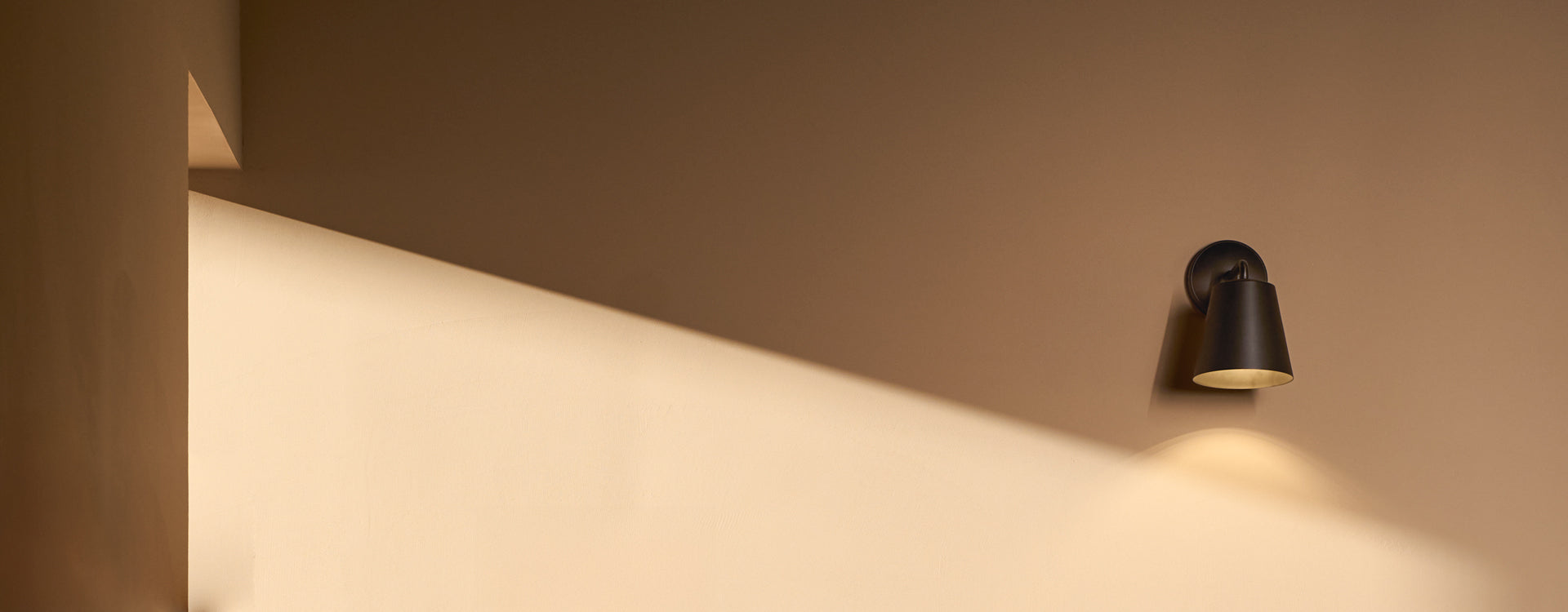 A sleek black wall lamp casts warm light against a soft beige wall, creating an elegant and modern ambiance.
