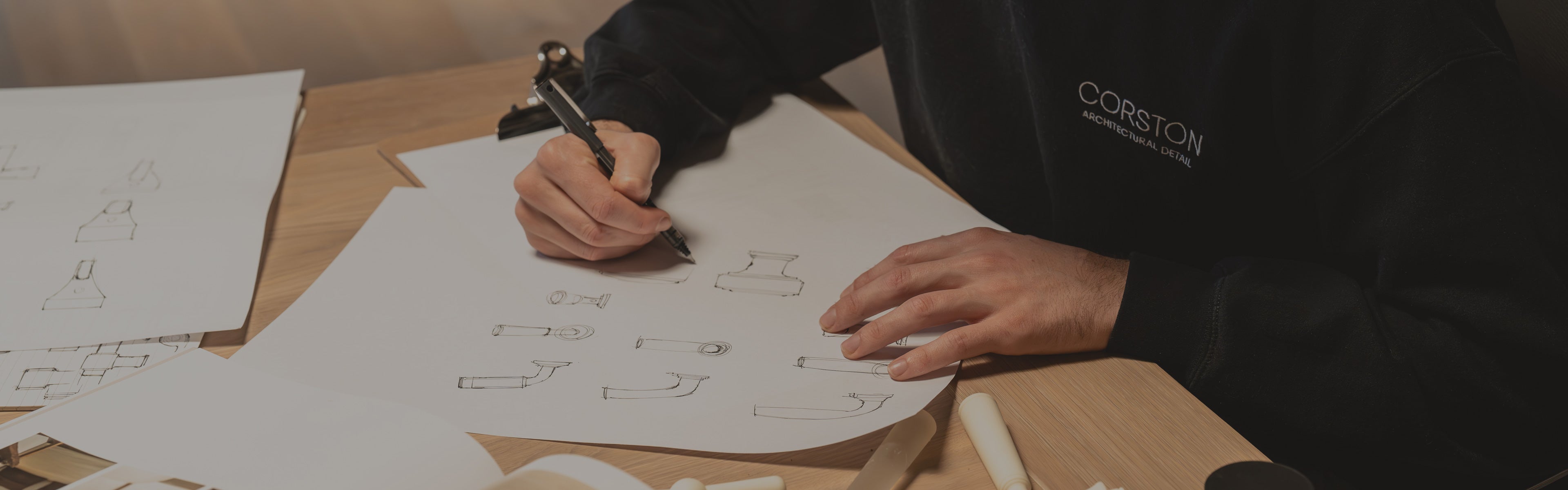 A person sketches designs on paper, promoting a trade program for design professionals. Includes options to apply or log in.
